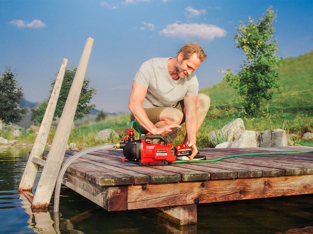 A man removes the Power X-Change battery from the Einhell AQUINNA battery garden pump.