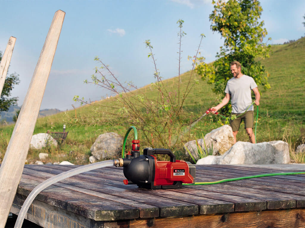 A man waters his garden with the help of the Einhell AQUINNA battery garden pump.